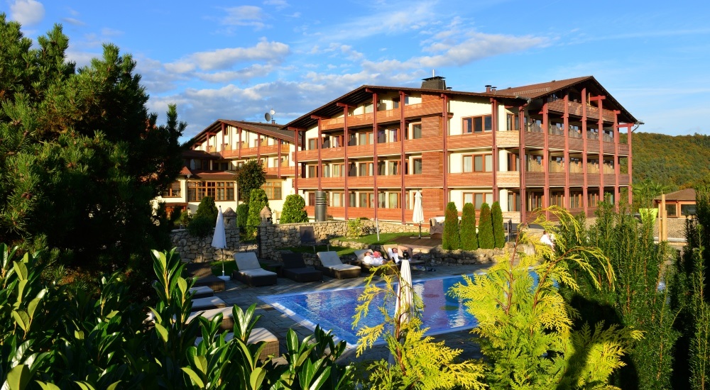 Aussenansicht des Hotels aufgenommen im Sommer. Im Vordergrund der Aussenpool, im Hintergrund der Hotelkomplex.
