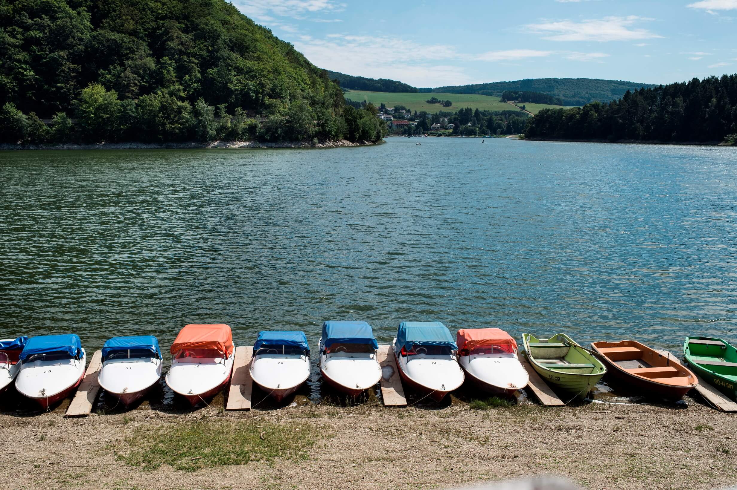 Im Vordergrund mehrere kleine Boote, die am Ufer des Diemelsees liegen. Der Blick richtet sich auf den Diemelsee. Im Hintergrund die grüne Landschaft.