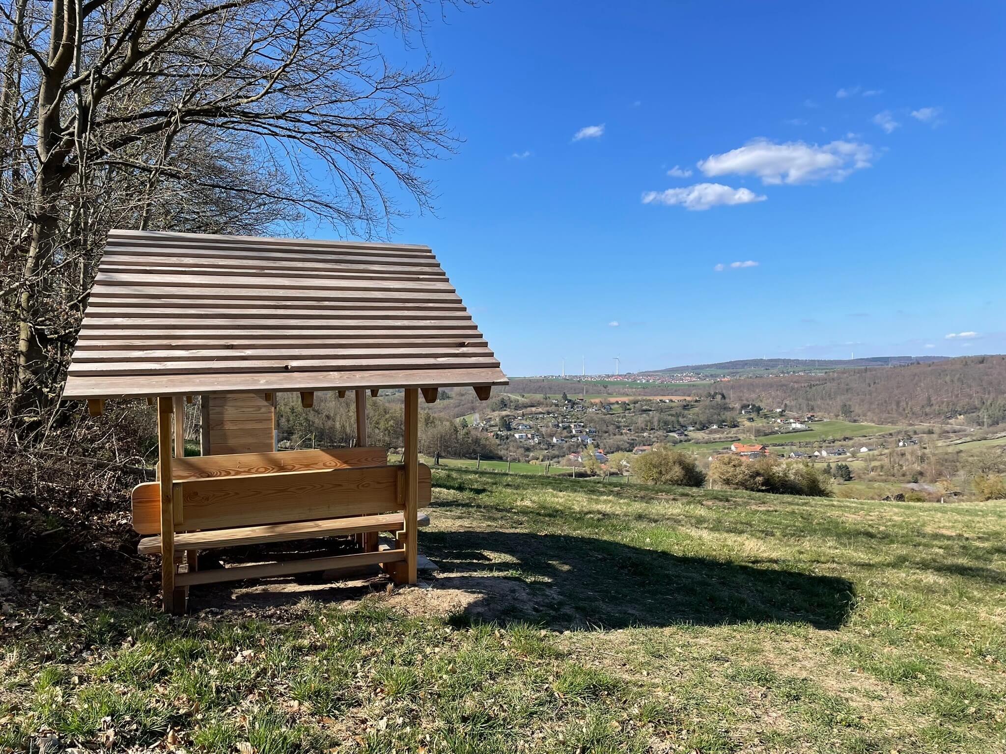 Eine überdachte Holzbank auf einer Lichtung mit Blick auf eine schöne Landschaft im Naturpark Kellerwald-Edersee.