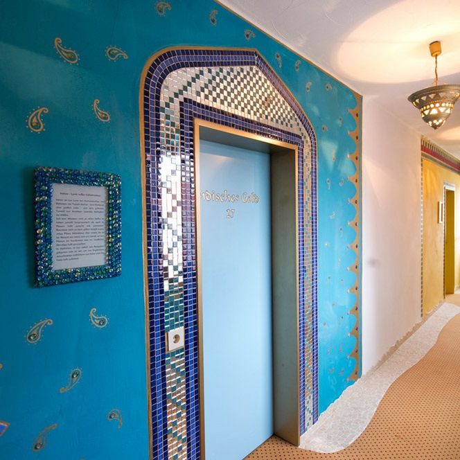 Der Flur im Hotel Goldflair am Rathaus ist orientalisch gestaltet mit blauer Wand und Mosaiksteinchen rund um die Zimmertür.