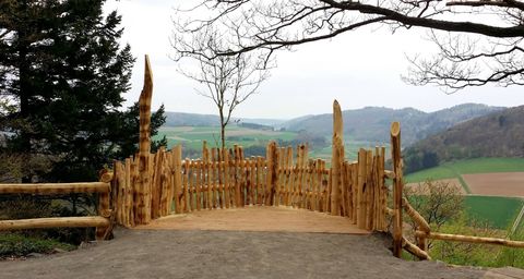 Eine Aussichtsplattform eingezäunt mit senkrecht stehenden Holzpfählen. Der Blick richtet sich in die Landschaft