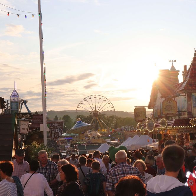 Viele Menschen auf einem Jahrmarkt mit Karussells, Riesenrad und einigen Ständen.