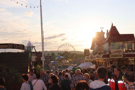 Viele Menschen auf einem Jahrmarkt mit Karussells, Riesenrad und einigen Ständen.