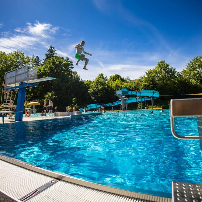 Das Schwimmbecken im Freibad Usseln mit Sprungbrett und kleiner Wasserrutsche im Sommer.