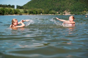Zwei Mädchen sind im Wasser und spritzen sich nass.