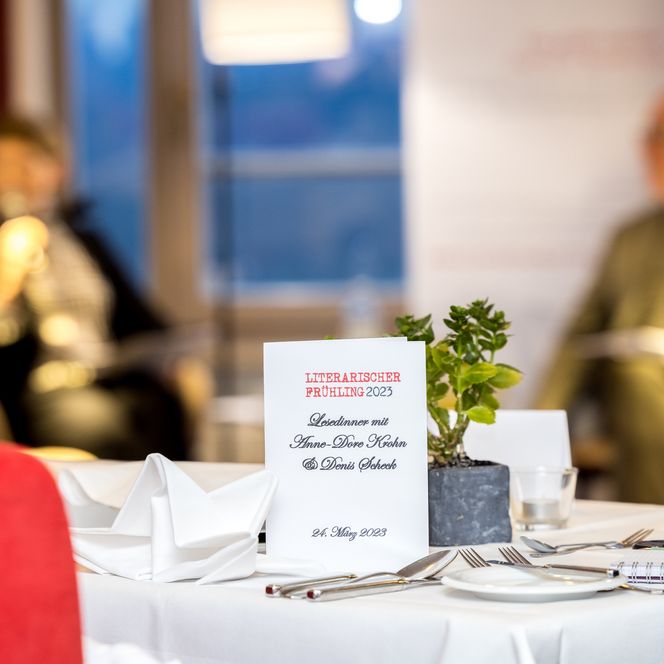 Ein Infoschild auf dem Literarischer Frühling 2023 Lesedinner steht. Das Schild steht auf einem eingedeckten Tisch.