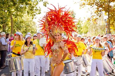 Eine Sambatänzerin mit Federn im Hintergrund die Musiker eines Samba Zuges.