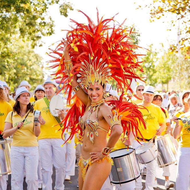 Eine Sambatänzerin mit Federn im Hintergrund die Musiker eines Samba Zuges.