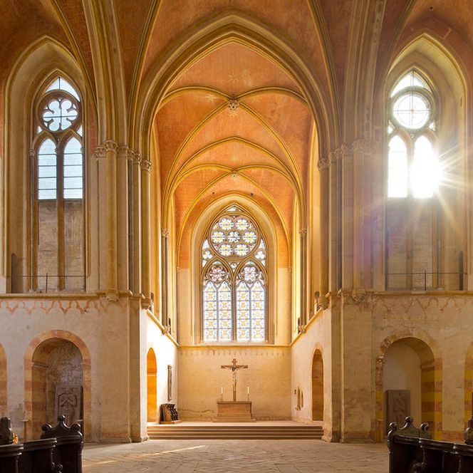 Innenraum der Klosterkirche Haina mit Blick auf Chor und Vierung. Weiter hinten zwei Kerzen, in der Mitte ein Kreuz.