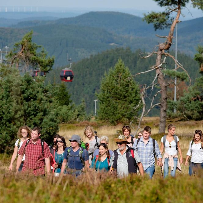 Eine Gruppe Wanderer mit Wanderausrüstung in der Natur. Im Hintergrund die Seilbahn des Ettelsberges.
