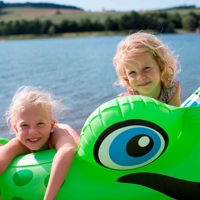 Zwei Mädchen halten sich an einem grünen Schwimmtier fest und baden im Wasser.