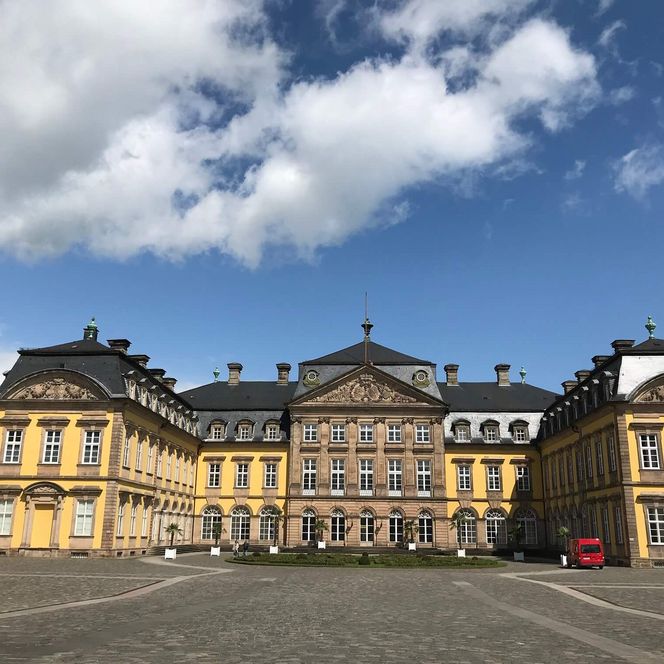 Das Bild zeigt das dreiflügelige Schloss Bad Arolsen von aussen unter blauem Himmel. Es zeigt die Ansicht vom Tor aus in den Schlosshof auf das gelbe Schloss.