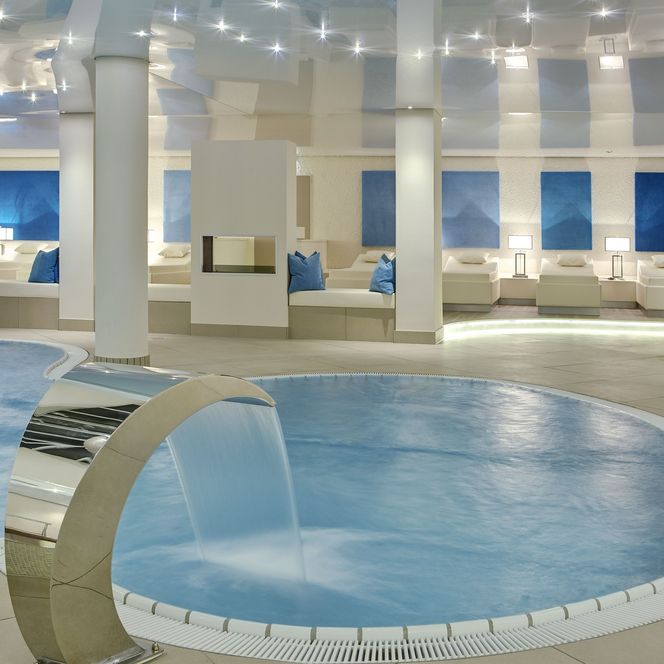 Spa-Bereich mit einigen Relaxliegen und einem kleinen Pool im Vordergrund. Alles in cremefarbenen Tönen gehalten.