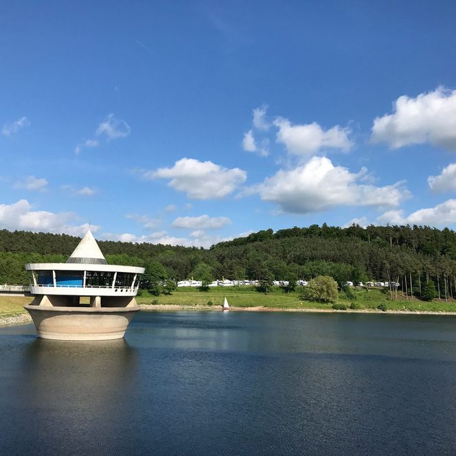Das Café befindet sich in einem runden Gebäude mit Spitze und ist über eine Brücke erreichbar. Es liegt im Twistesee. Im Hintergrund ist der Wohnmobilhafen zu sehen.