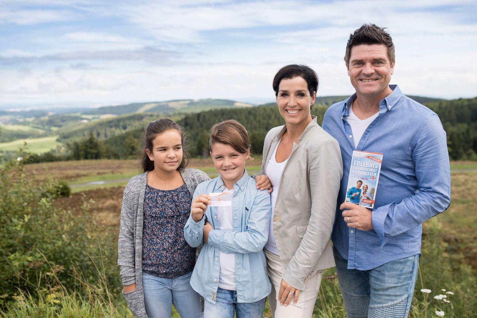 Eine Familie (ein Mann, eine Frau und zwei Kinder) stehen in der Natur und halten die MeineCardPlus und eine Infobroschüre in den Händen.