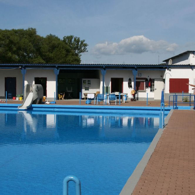Das Freibad in Twistetal im Ortsteil Twiste verfügt über ein solarbeheiztes 25-Meter-Becken. Auf dem Bild sieht man das Becken sowie die dahinterliegenden Kabinen sowie Tische und Stühle für die Gäste.