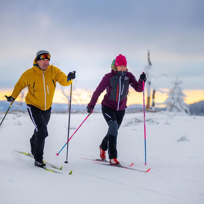 Paar beim Langlauf in Willingen auf einer verschneiten Loipe, umgeben von winterlicher Waldlandschaft und glitzerndem Schnee.
