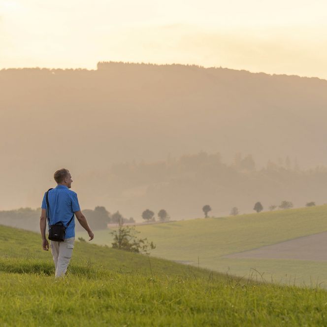 Ein Mann, der auf einer grünen Wiese im stimmungsvollen Licht läuft. Im Hintergrund die Willinger Hügel.