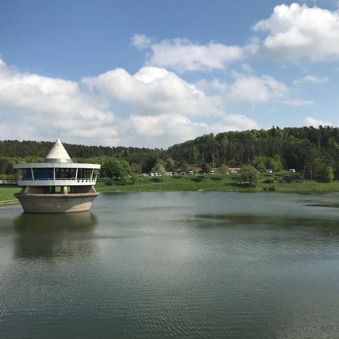 Das Café befindet sich in einem runden Gebäude mit Spitze und ist über eine Brücke erreichbar. Es liegt im Twistesee. Im Hintergrund ist der Wohnmobilhafen zu sehen. 