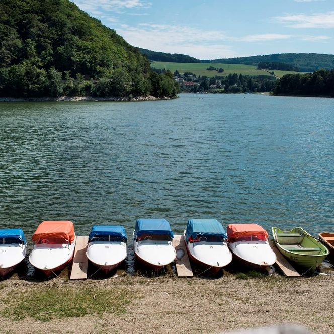 Im Vordergrund mehrere kleine Boote, die am Ufer des Diemelsees liegen. Der Blick richtet sich auf den Diemelsee. Im Hintergrund die grüne Landschaft.