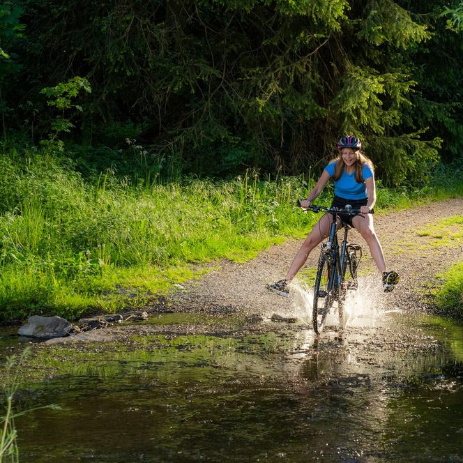 Ein Mädchen fährt mit ihrem Trekkingrad mit ausgestreckten Beinen in die seichte Eder
