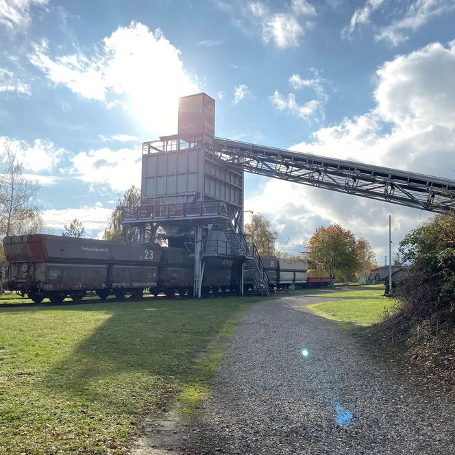 Ein Förderband und ein Zug mit mehreren Loren stehen draußen vor dem Braunkohlemuseum in Borken.