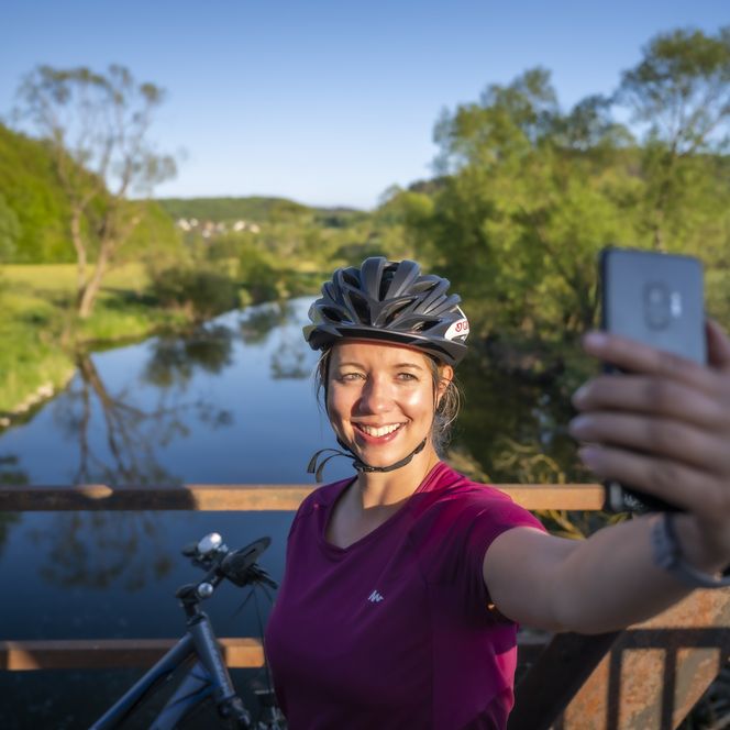 Eine Radlerin steht auf der Brücke über die Eder bei Hatzfeld-Holzhausen und macht ein Selfie