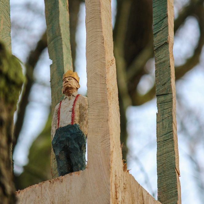 Eine kleine geschnitzte Holzfigur steht an einem Wanderweg