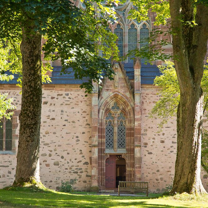 Hinter Bäumen gelegen befindet sich die relativ kleine Eingangstür zum imposanten Kloster.