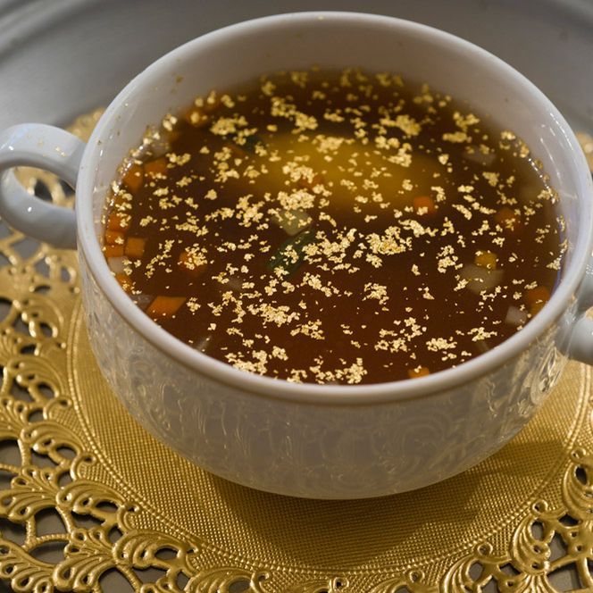 Eine Suppenterrine gefüllt mit Suppe und Goldflitter auf einem goldenen Unterteller