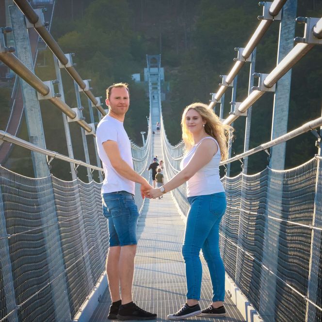 Ein Mann und eine Frau halten sich an der Hand und stehen auf der Hängebrücke (dem Skywalk).