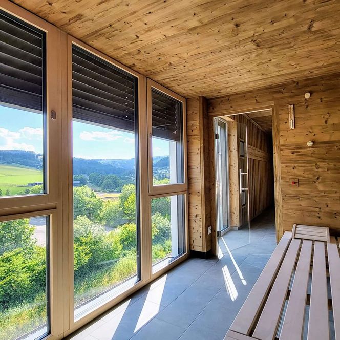 Saunabereich mit großen Panoramafenstern und Blick auf grüne Hügel im Mountain View Hotel Willingen