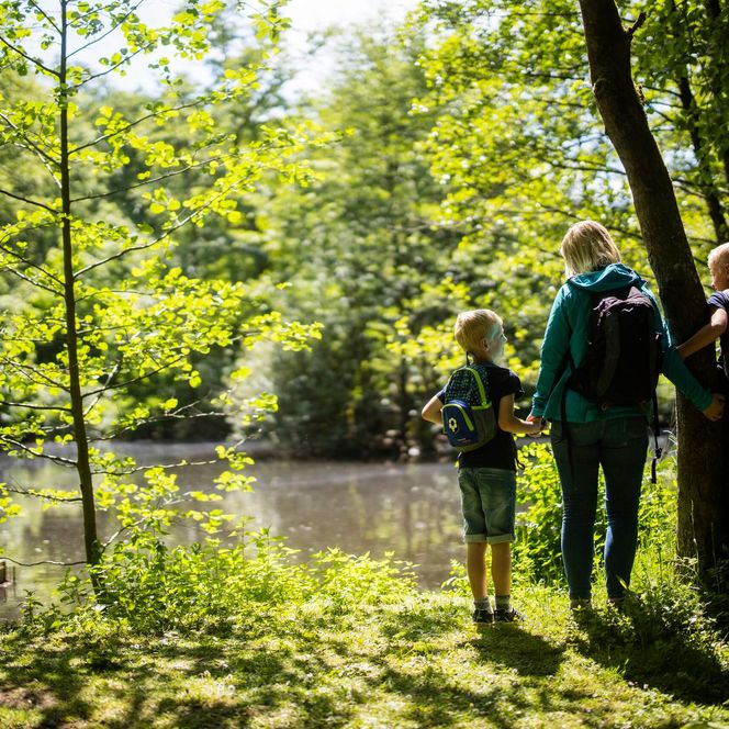 Eine Frau und zwei Kinder mit Rucksäcken stehen am Ufer des Diemelsees.